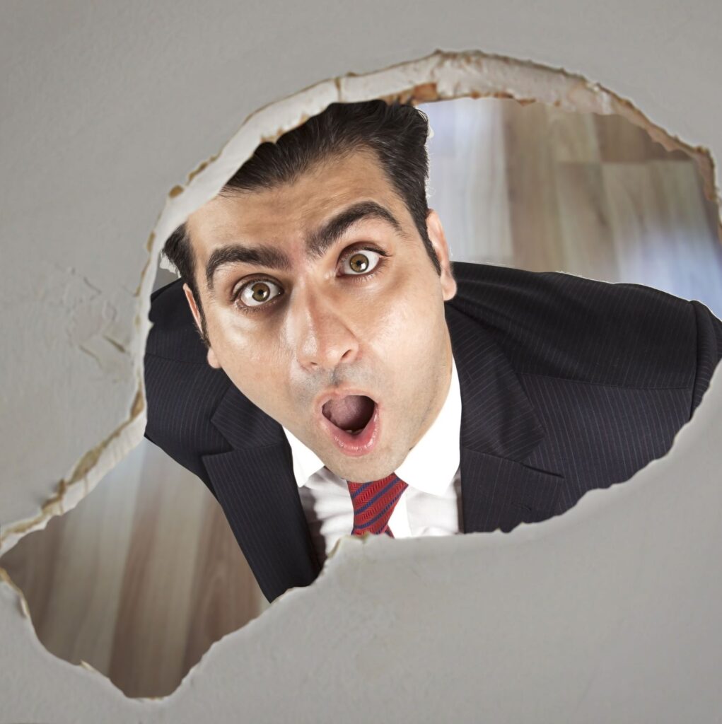 man looking up at roof leak hole looking shocked