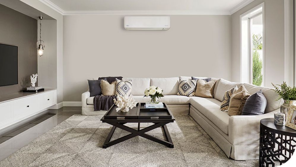 A modern living room with a white Fujitsu heat pump installed above a beige sectional sofa.