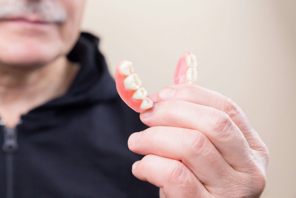 An older man holding broken dentures, highlighting the need for urgent denture repairs in Te Awamutu.