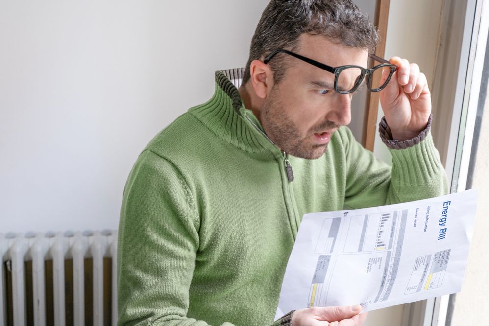 Man looking shocked at high energy bill while standing next to radiator, highlighting winter heating costs in Ashburton homes.