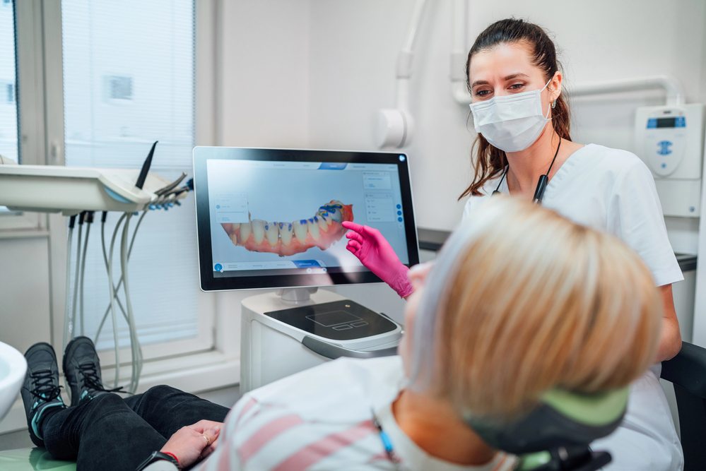 An orthodontist showing a patient a 3D digital scan of their teeth on screen at a clinic, discussing clear aligner treatment options.