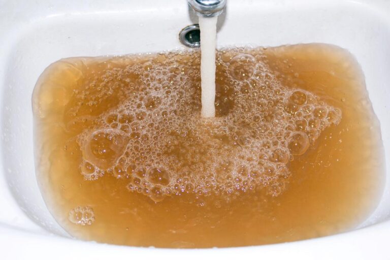 Brown, rusty water flowing from a tap into a white sink, showing signs of corrosion and plumbing issues common in coastal homes.