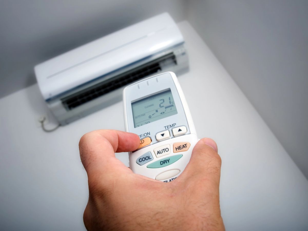 A hand holding a heat pump remote set to 21 degrees while operating a wall-mounted heat pump unit.